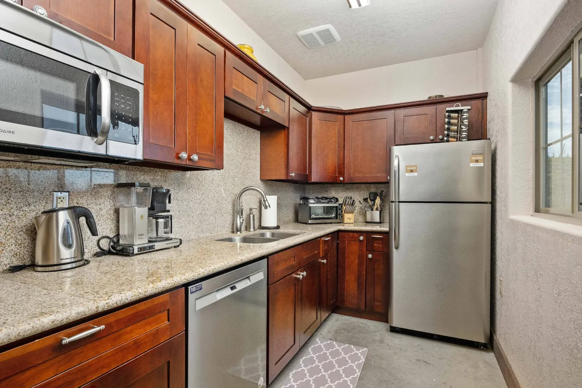 A warmly lit kitchen with granite countertops, stainless steel appliances, wood cabinetry, and a kitchen sink. The countertops are spacious enough for preparing meals or sharing a casual conversation, and the overall design feels welcoming and functional.