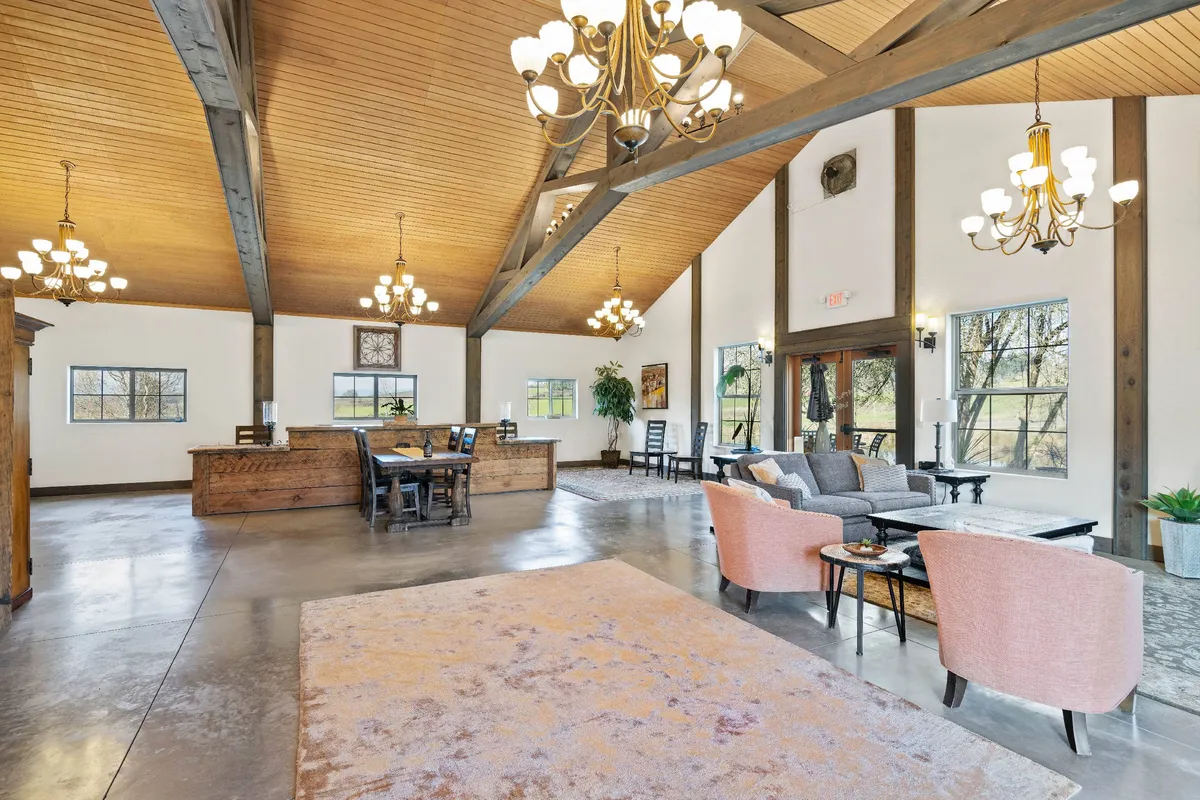 A warm, integrated space combining a dining table, sofa seating, and large windows. The glowing chandeliers and fireplace accentuate the cozy, sociable vibe, while sunlight pours in, emphasizing year-round appeal.