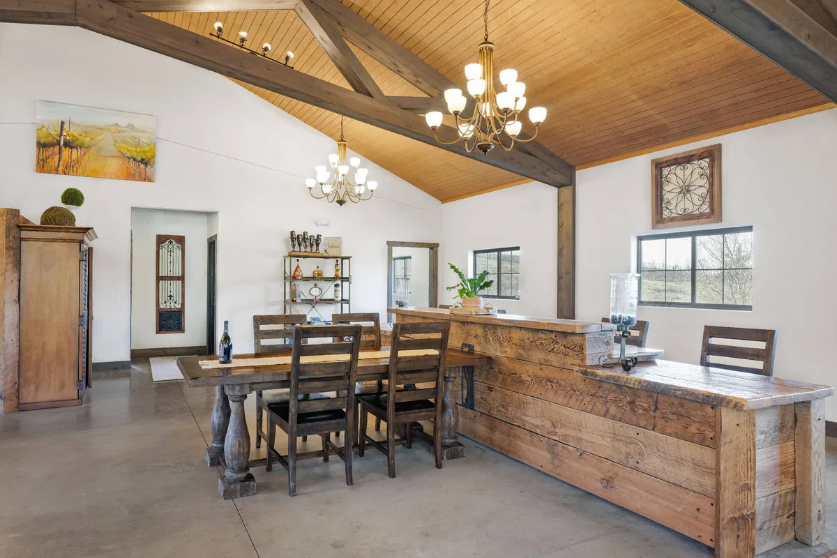 A large wooden dining table sits beneath a chandelier, with the open kitchen area visible in the background. Rustic shelving adds charm, and the space feels ready for both intimate dinners and lively gatherings.
