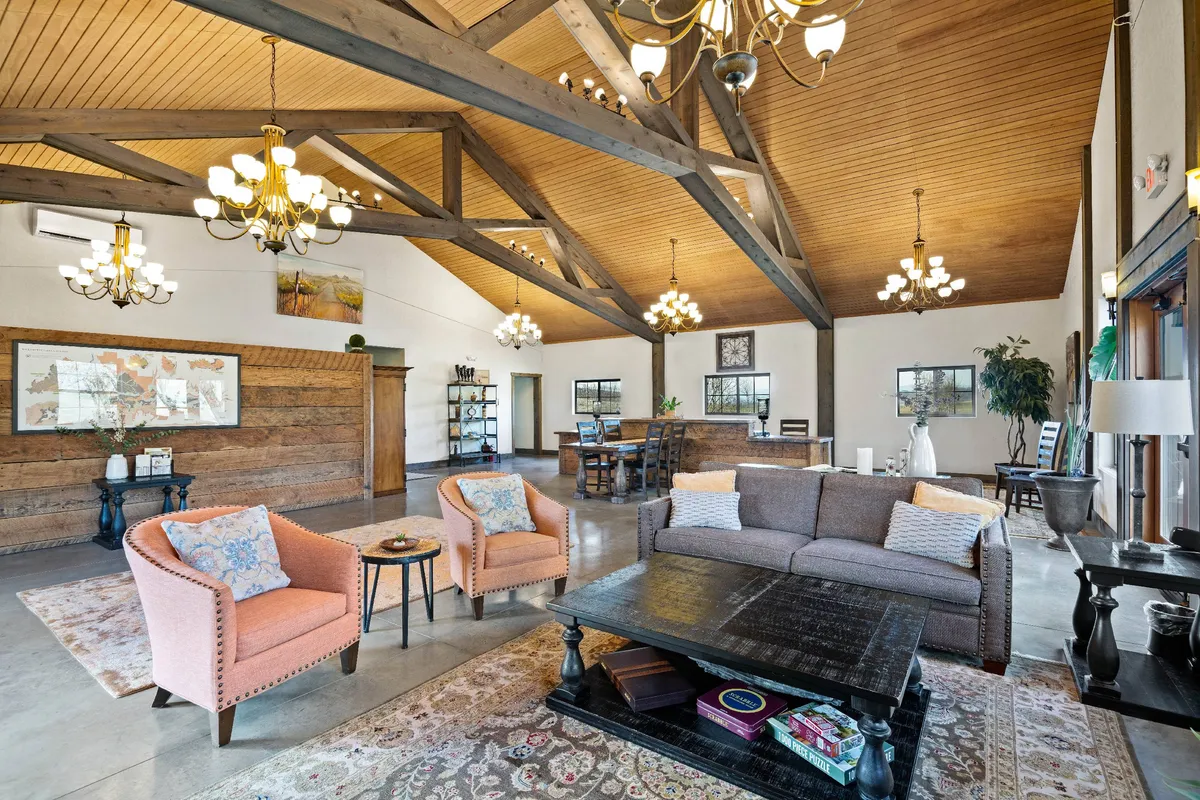 A cozy living area with plush sofas, a decorative rug, a wooden beam ceiling, and eye-catching chandeliers. Ample seating provides space for groups to relax, play games, or enjoy a glass of wine. The room feels welcoming and designed for social connection.